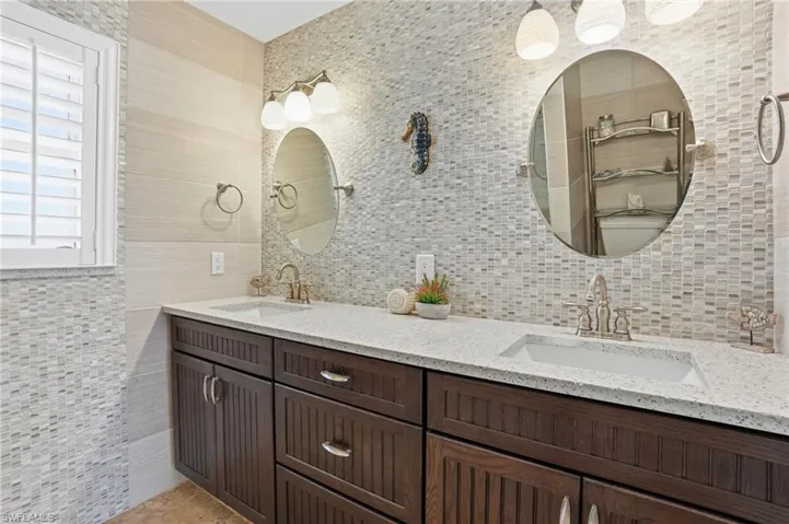 Full bath with tile walls, double vanity, and decorative backsplash