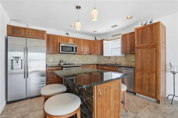 Kitchen featuring a kitchen bar, stainless steel appliances, dark stone countertops, hanging light fixtures, and a kitchen island