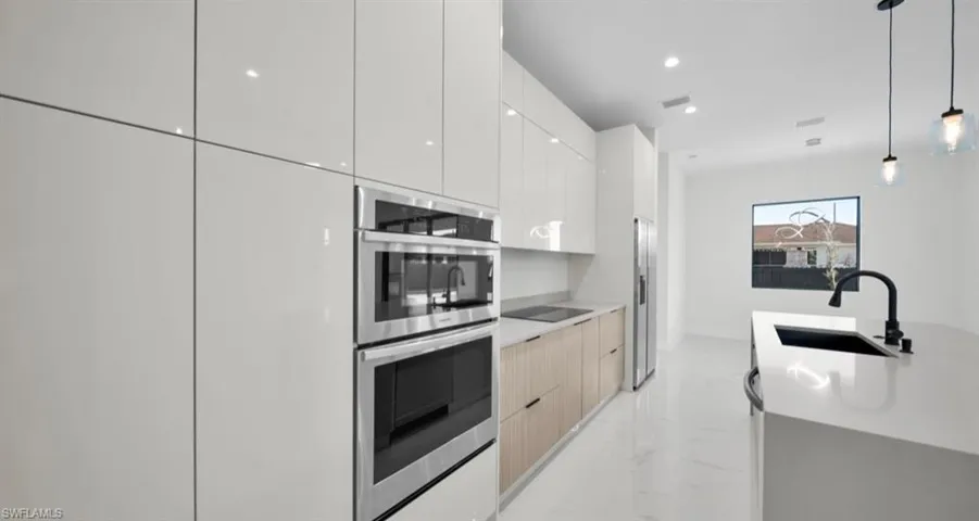 Kitchen featuring decorative light fixtures, modern cabinets, light marble finish floors, stainless steel appliances, and recessed lighting