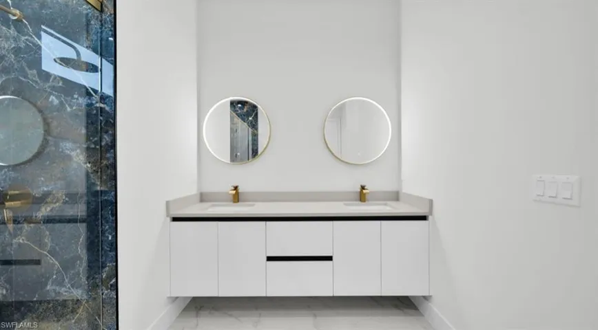 Bathroom with double vanity, light marble finish flooring, and a marble finish shower