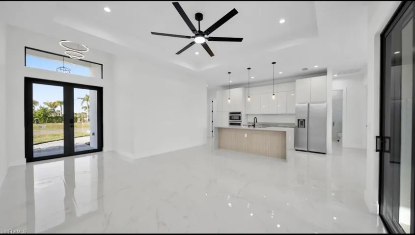Kitchen featuring open floor plan, stainless steel fridge, a tray ceiling, a center island with sink, and recessed lighting