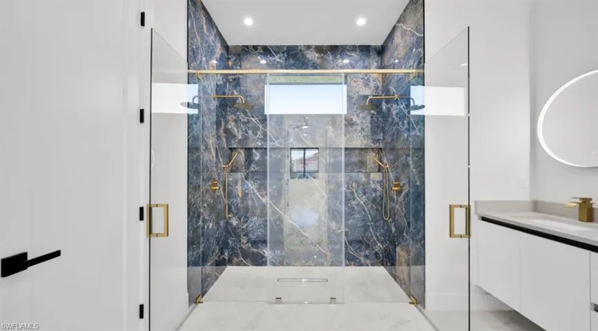 Bathroom with a marble finish shower, marble tiled floors, vanity, and recessed lighting
