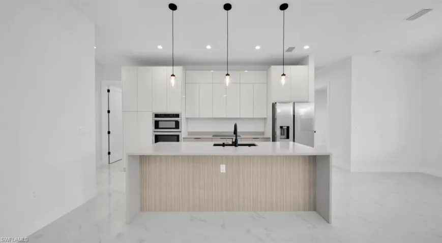 Kitchen featuring modern cabinets, decorative light fixtures, light stone counters, stainless steel appliances, and white cabinets