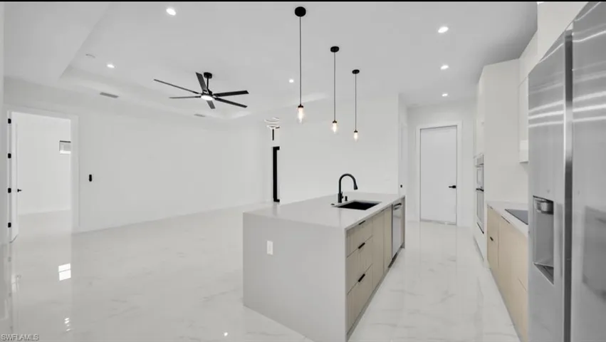 Kitchen featuring modern cabinets, appliances with stainless steel finishes, recessed lighting, decorative light fixtures, and light stone countertops