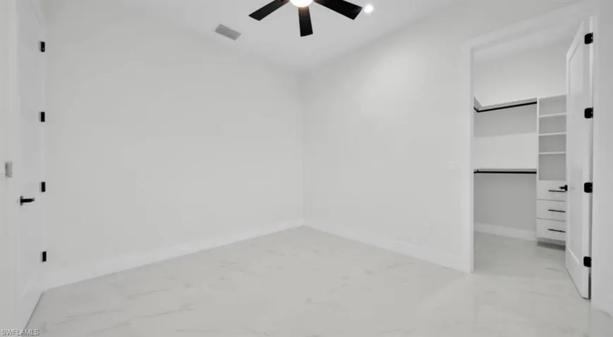Unfurnished bedroom featuring a walk in closet, light marble finish floors, and a ceiling fan