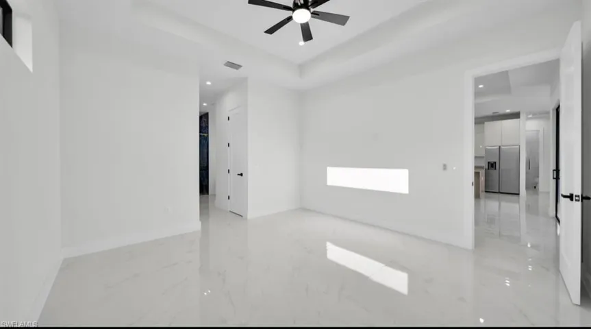 Unfurnished room featuring a tray ceiling, recessed lighting, light marble finish flooring, and ceiling fan