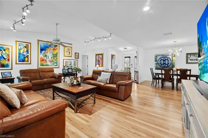 Living room with ceiling fan with notable chandelier, track lighting, and light hardwood / wood-style floors