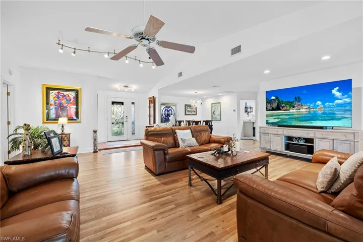 Living room featuring vaulted ceiling, ceiling fan with notable chandelier, track lighting, and light hardwood / wood-style floors