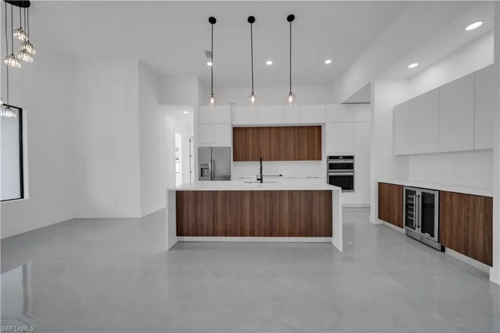 Kitchen with modern cabinets, appliances with stainless steel finishes, beverage cooler, a sink, and light countertops