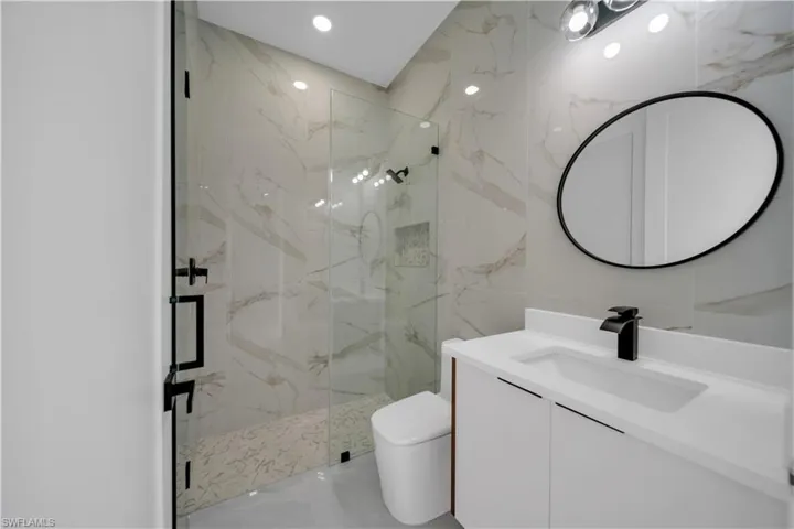 Full bathroom with vanity, a marble finish shower, marble tiled flooring, toilet, and tile walls