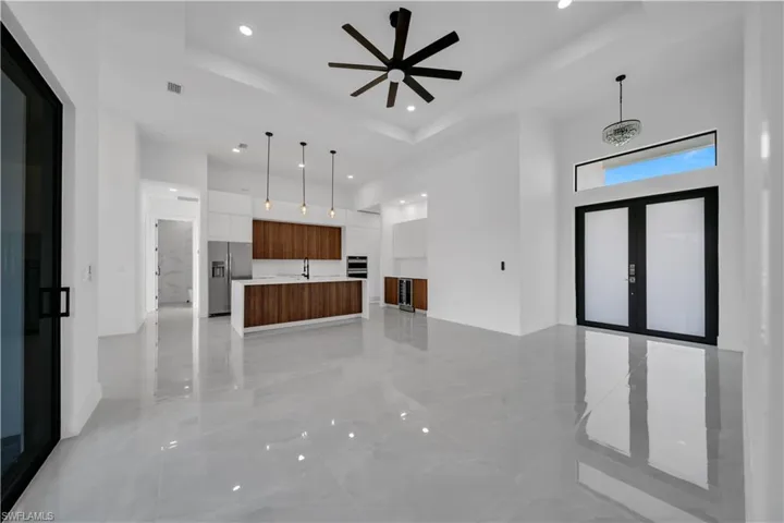 Unfurnished living room with a high ceiling, a tray ceiling, recessed lighting, ceiling fan, and a sink