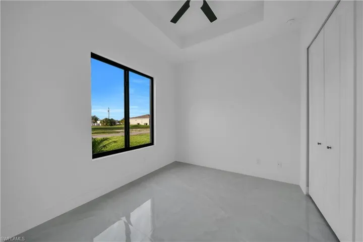 Unfurnished bedroom featuring a closet, a raised ceiling, a ceiling fan, and light marble finish floors