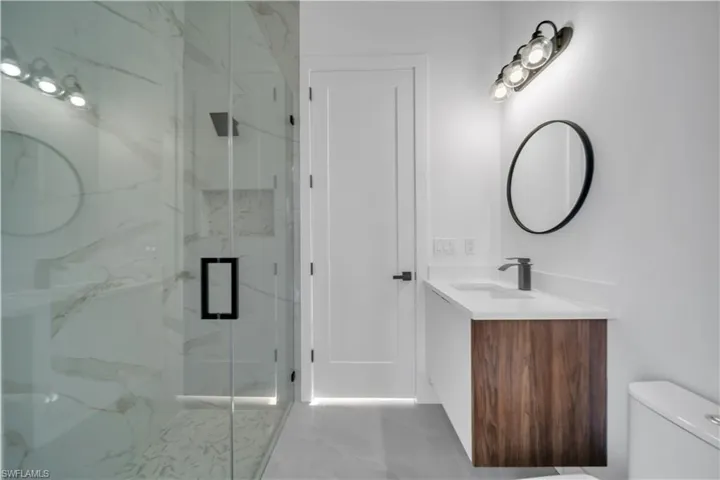 Bathroom with vanity, toilet, a marble finish shower, and marble finish flooring