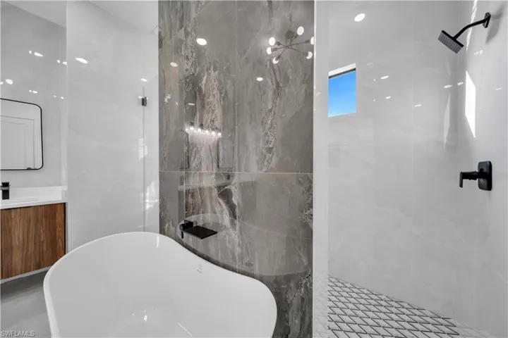 Bathroom with vanity, a freestanding tub, tiled shower, and tile walls