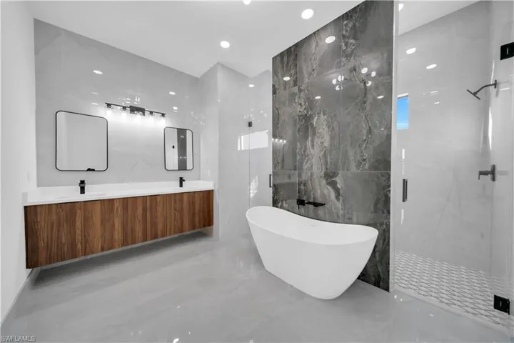 Bathroom with a marble finish shower, tile walls, marble tiled floors, a freestanding bath, and double vanity