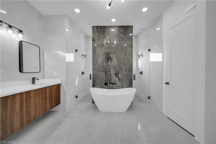 Bathroom featuring tile walls, a stall shower, a freestanding tub, marble tiled flooring, and vanity
