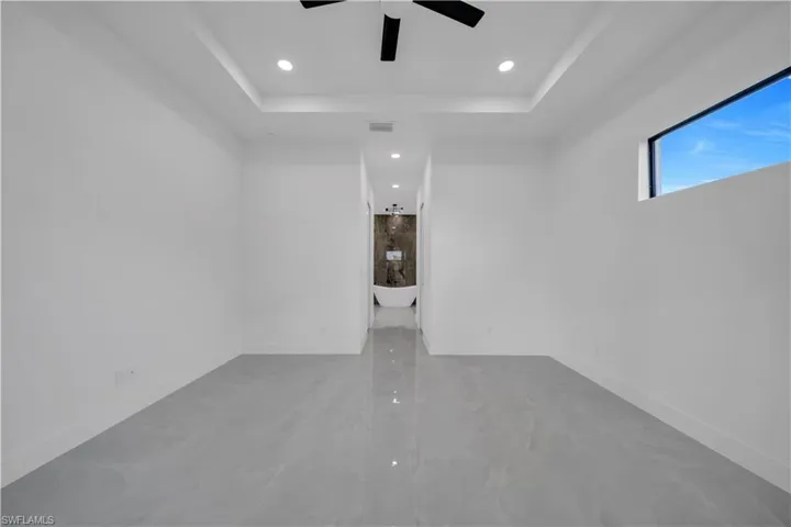 Empty room with a raised ceiling, ceiling fan, recessed lighting, marble finish flooring, and baseboards