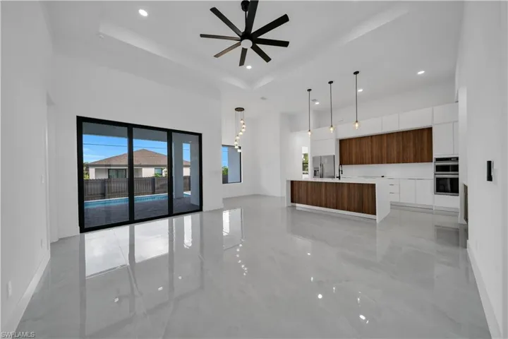 Unfurnished living room with a raised ceiling, ceiling fan, light marble finish floors, a towering ceiling, and recessed lighting