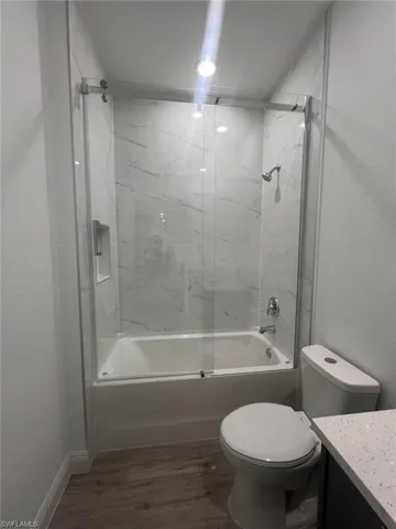 Full bathroom with enclosed tub / shower combo, vanity, toilet, and hardwood / wood-style floors