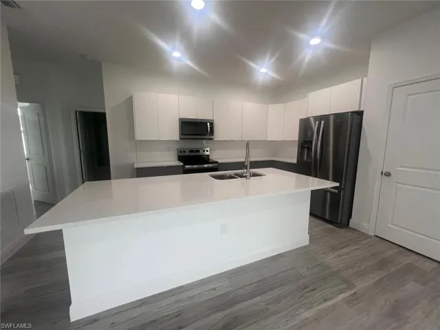 Kitchen featuring an island with sink, stainless steel appliances, wood-type flooring, sink, and white cabinetry