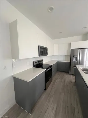 Kitchen featuring white cabinets, dark wood-type flooring, backsplash, and stainless steel appliances