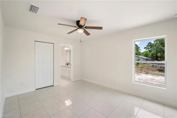 Unfurnished bedroom featuring ceiling fan, a closet, ensuite bath, and light tile floors