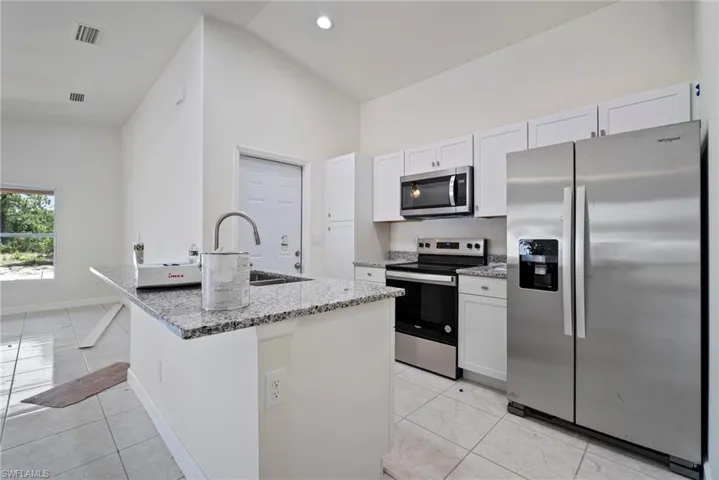 Kitchen with appliances with stainless steel finishes, white cabinets, light tile flooring, and a kitchen island with sink