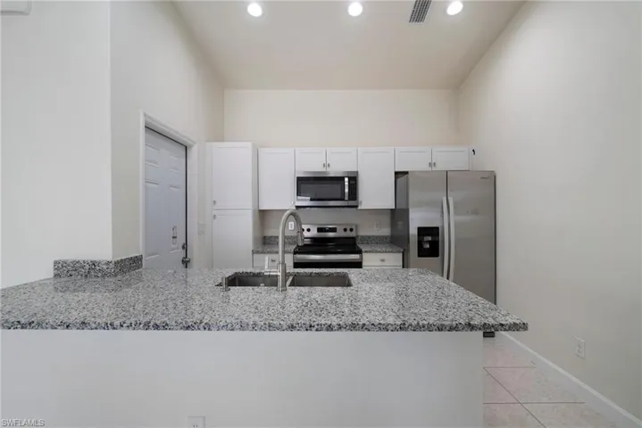 Kitchen with light stone countertops, kitchen peninsula, sink, white cabinets, and appliances with stainless steel finishes