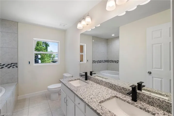 Bathroom featuring dual vanity, a relaxing tiled bath, toilet, and tile floors