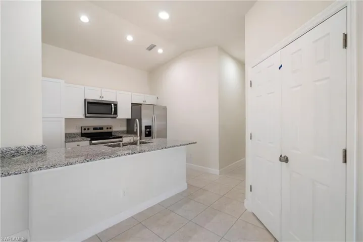 Kitchen with light stone countertops, white cabinets, sink, light tile floors, and appliances with stainless steel finishes