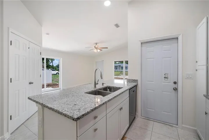 Kitchen with light stone countertops, stainless steel dishwasher, sink, ceiling fan, and light tile floors