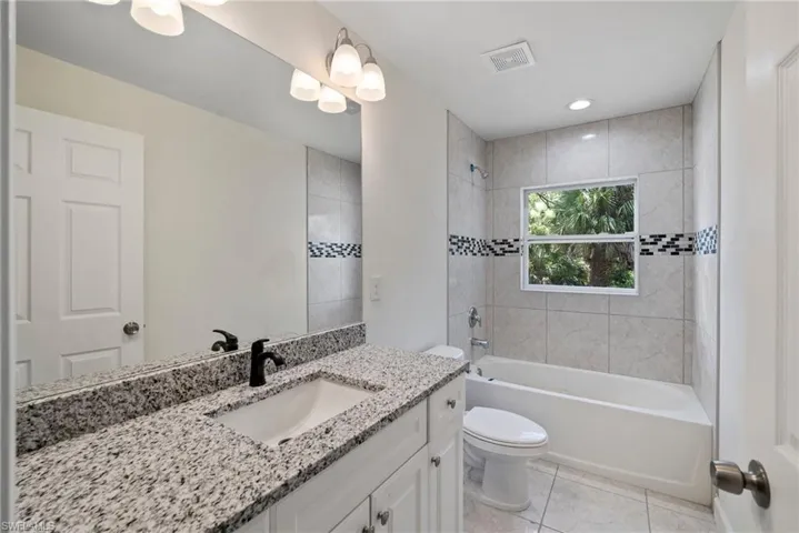 Full bathroom with tile floors, vanity, toilet, and tiled shower / bath combo