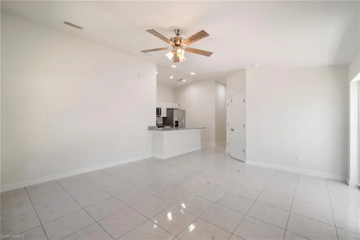 Unfurnished living room featuring light tile flooring, ceiling fan, and vaulted ceiling