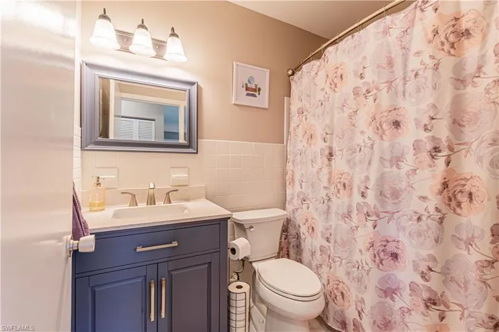 Bathroom with vanity, tasteful backsplash, walk in shower, tile walls, and toilet