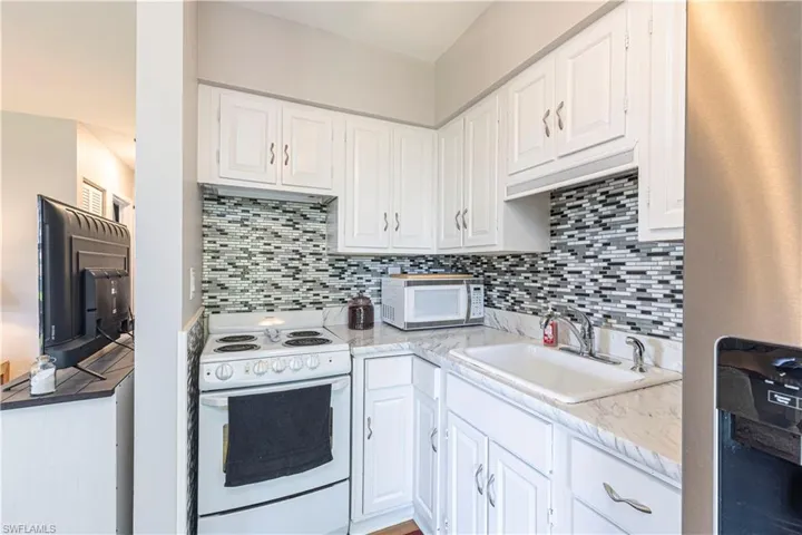 Kitchen featuring white cabinets, white appliances, tasteful backsplash, and sink