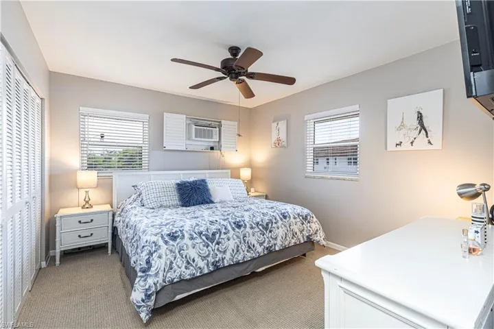 Carpeted bedroom with multiple windows, an AC wall unit, ceiling fan, and a closet