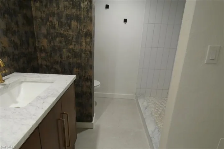 Modern bathroom featuring a vanity with a white countertop and gold-finish faucet, a decorative accent wall, a shower with vertical white subway tile, and a pebble-stone shower floor