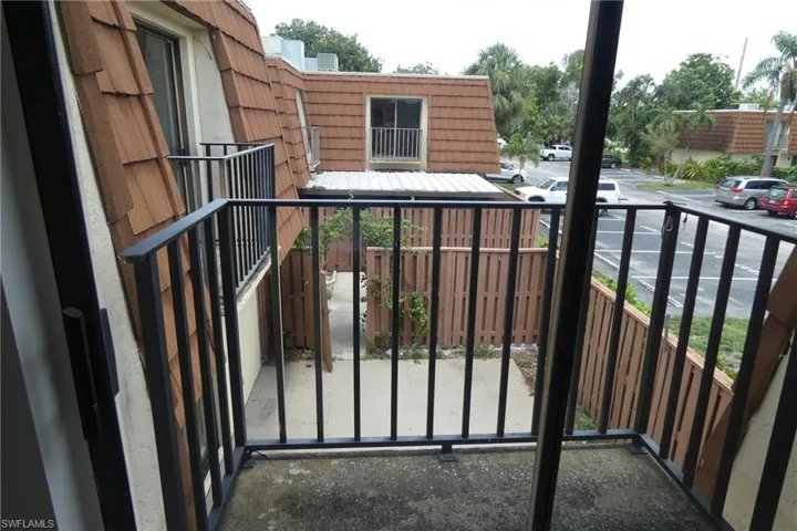 Private balcony with dark metal railings overlooking a fenced courtyard and parking area