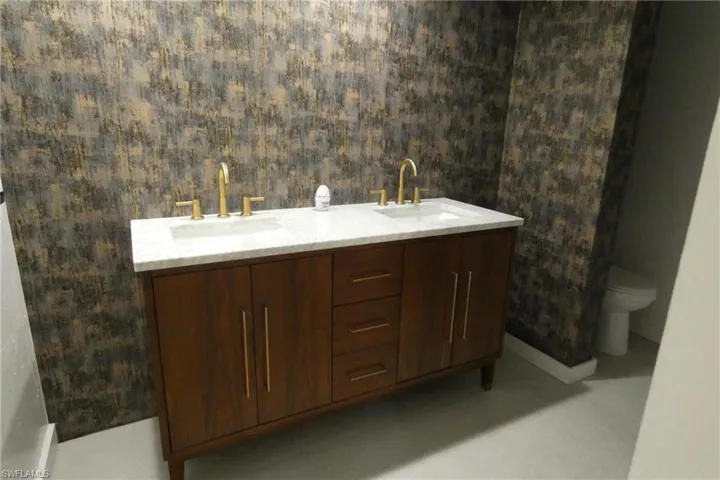 Dual vanity featuring a wood-finish cabinet, gold-tone hardware, and a white countertop