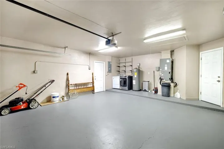 Garage featuring heating unit, electric panel, independent washer and dryer, a garage door opener, and electric water heater