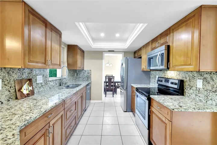 Kitchen with light tile patterned flooring, appliances with stainless steel finishes, sink, a tray ceiling, and light stone countertops