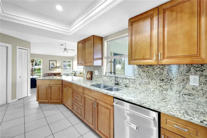 Kitchen with sink, stainless steel dishwasher, light stone counters, and a tray ceiling