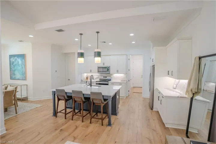 Kitchen with light hardwood / wood-style flooring, white cabinetry, appliances with stainless steel finishes, and decorative light fixtures