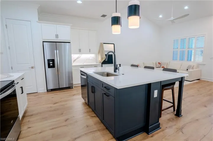 Kitchen with appliances with stainless steel finishes, hanging light fixtures, sink, and light hardwood / wood-style flooring