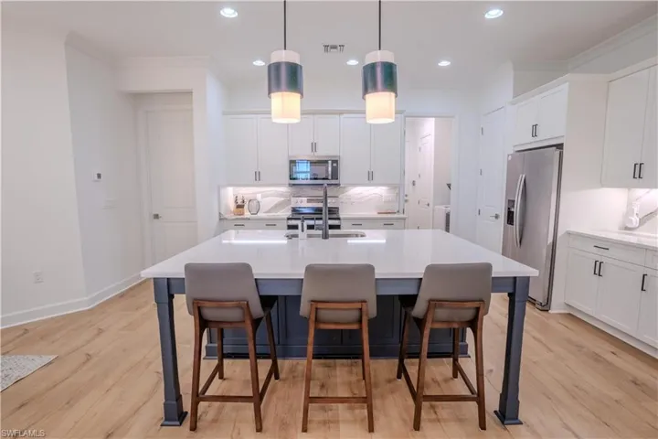 Kitchen with stainless steel appliances, light hardwood / wood-style floors, hanging light fixtures, and sink