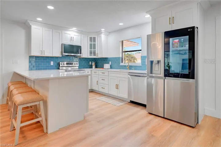 Kitchen with appliances with stainless steel finishes, sink, white cabinets, a breakfast bar, and light hardwood / wood-style floors