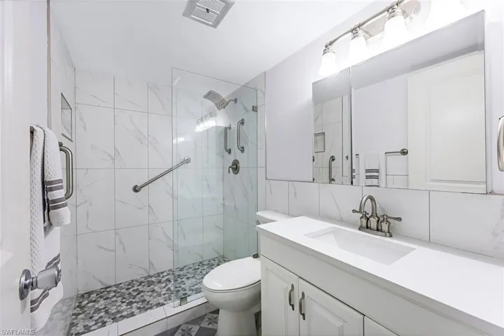 Bathroom featuring vanity, walk in shower, tile walls, toilet, and tile patterned flooring