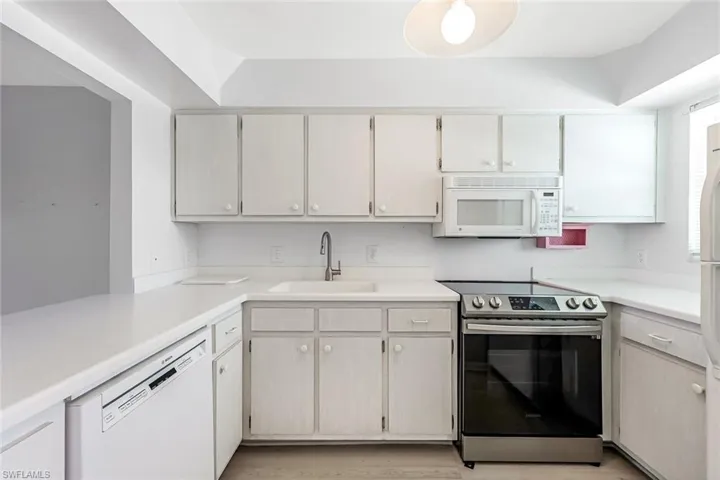 Kitchen featuring white cabinetry, a tray ceiling, white appliances, sink, and light hardwood / wood-style floors