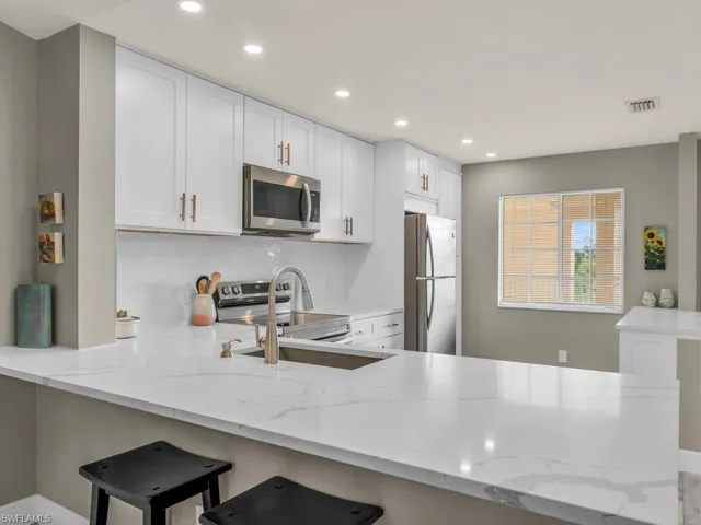 Kitchen with white cabinets, light stone counters, stainless steel appliances, and kitchen peninsula