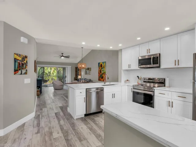 Kitchen with hanging light fixtures, light hardwood / wood-style flooring, appliances with stainless steel finishes, white cabinetry, and kitchen peninsula